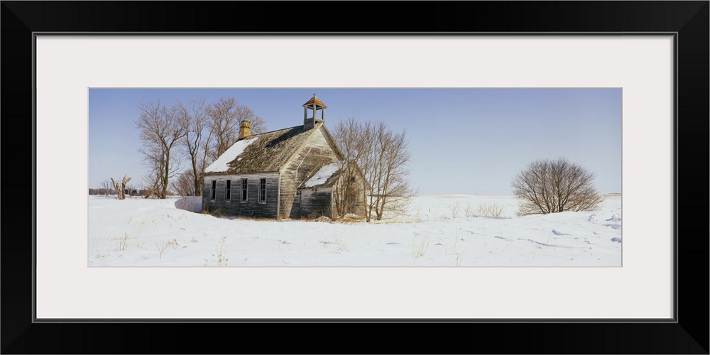 A run down building is surrounded by snow covered land and bare trees.