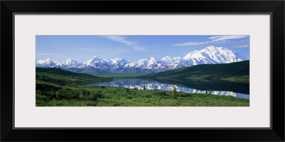 Panoramic photo of green fields surrounding a lake with snowy mountains in the distance.