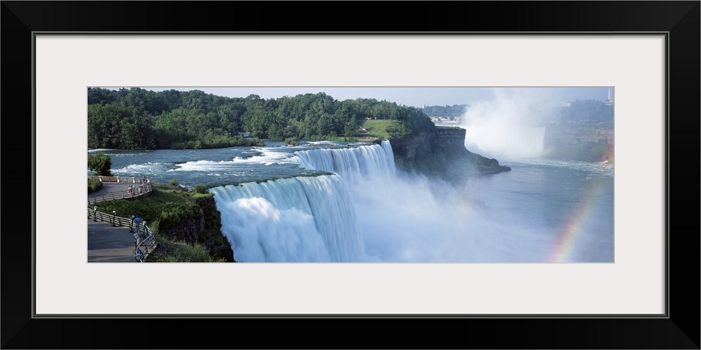 An elongated view of Niagara Falls with a sliver of a rainbow just to the right of the falls.