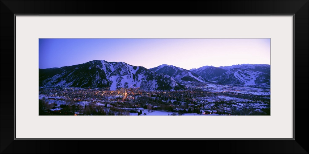 Long panoramic photo of Aspen Colorado at dust nestled in the valley of the snow covered mountains.