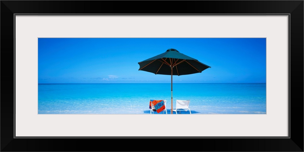 Two beach chairs under an umbrella in front of the ocean in the sand on the Turks and Caicos Islands.