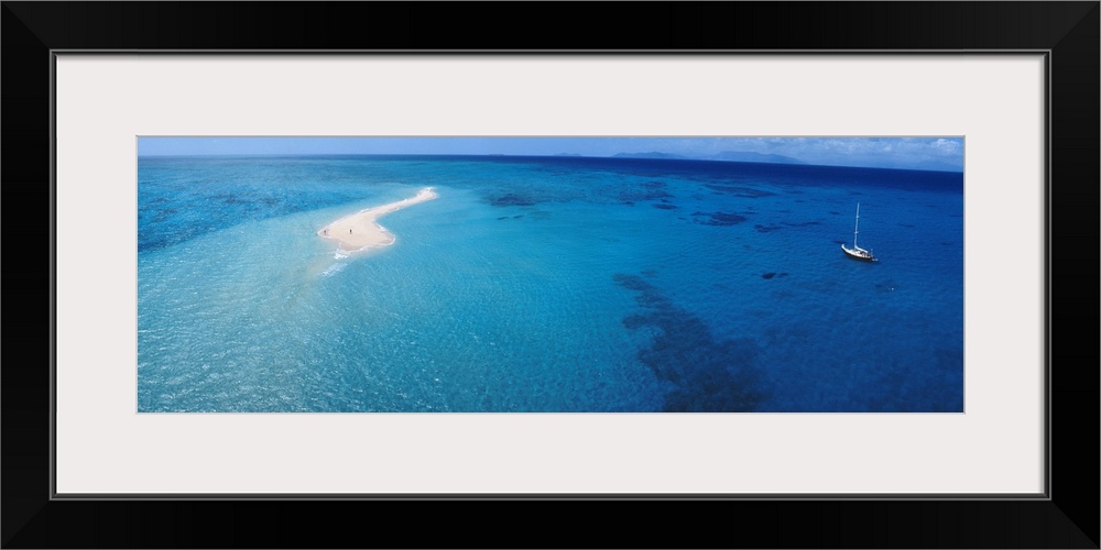 Panoramic, aerial photograph of clear blue waters over the Great Barrier Reef, a single sailboat in the water, in Queensla...