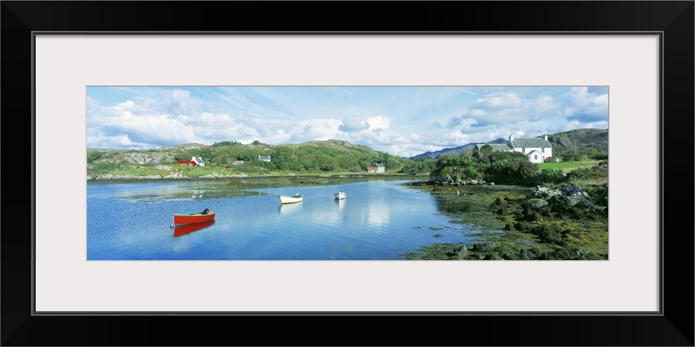 Panoramic photograph of canoes in the water with land and houses in the distance under a cloudy sky.