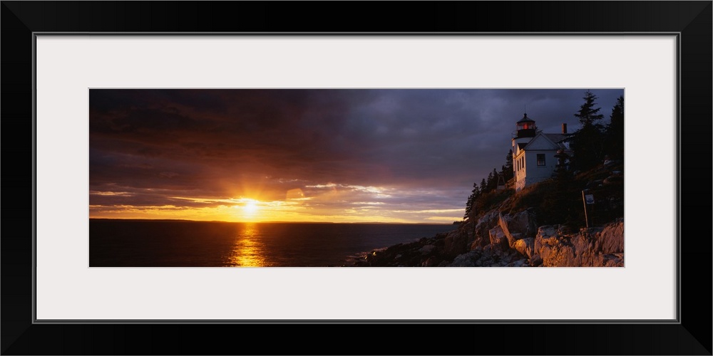 Large panoramic shot of a sun setting over a harbor with a house on a cliff just to the right.