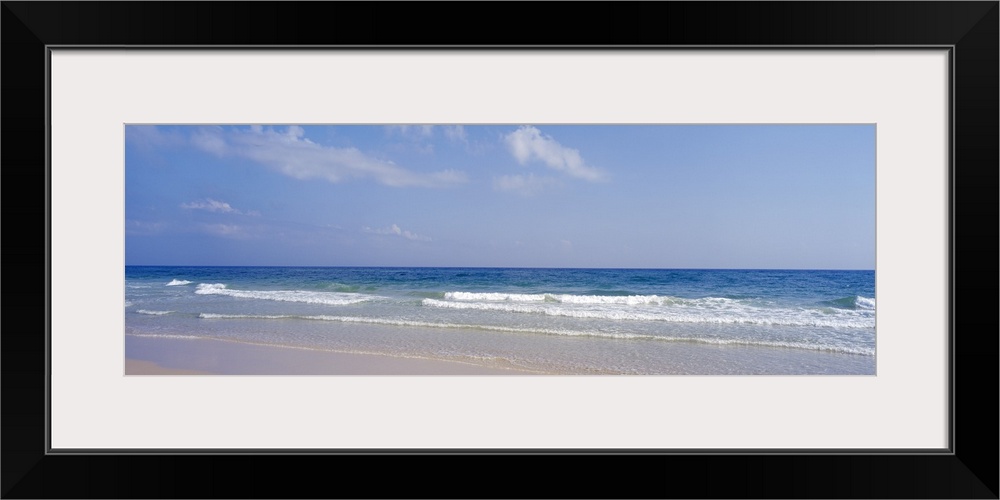 Docor perfect for the home or office of a panoramic shot of a beach with waves coming in and a soft blue sky just above.