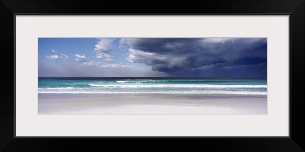 Panoramic photo print of an ocean with crashing waves and blue skies on the left and storm clouds on the right.