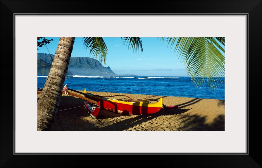Oversize wall art of a landscape photograph of a sailboat pulled up the shore and resting in the shade of a palm tree with...