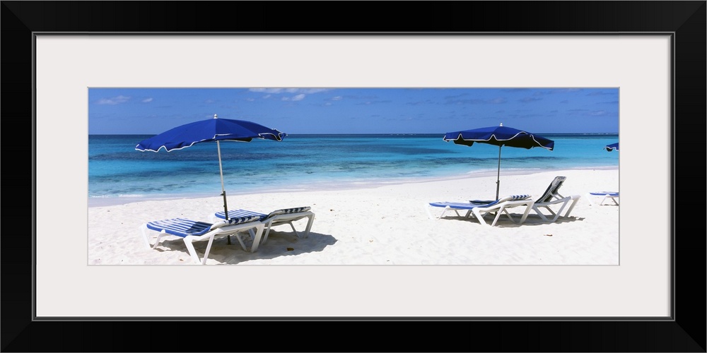 Beach chairs and umbrellas are pictured in panoramic view along the beach and close to the ocean.