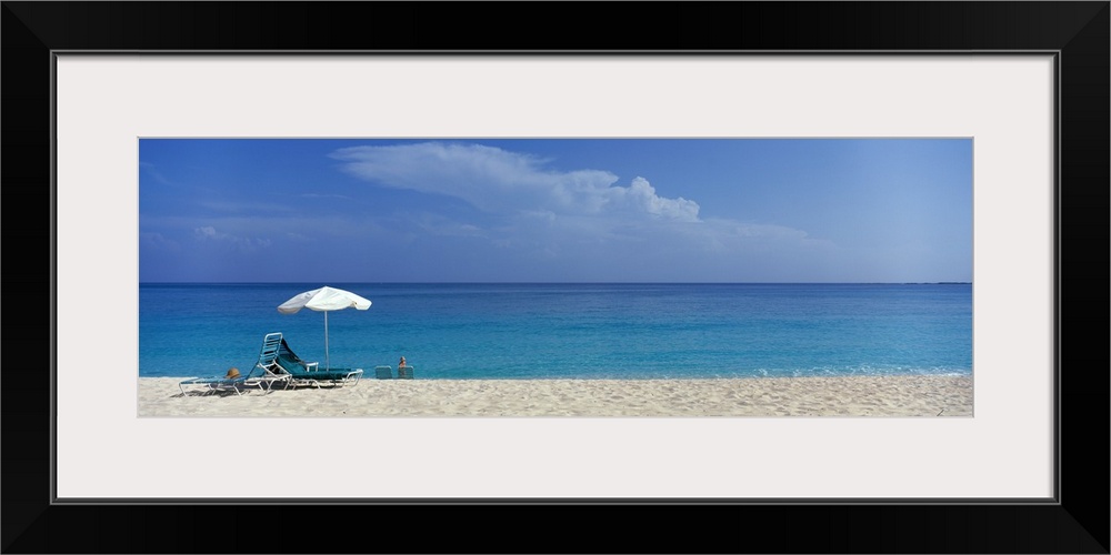 Panoramic photograph of beach chairs and umbrella on sand with calm ocean in the distance.