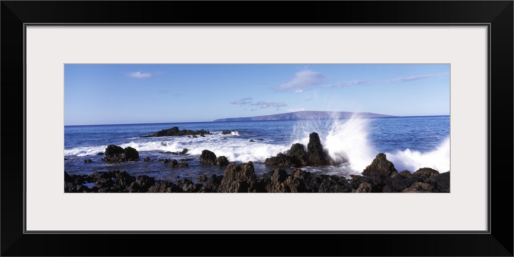 This panoramic photograph shows a wave breaking on the volcanic rock on the island shore.