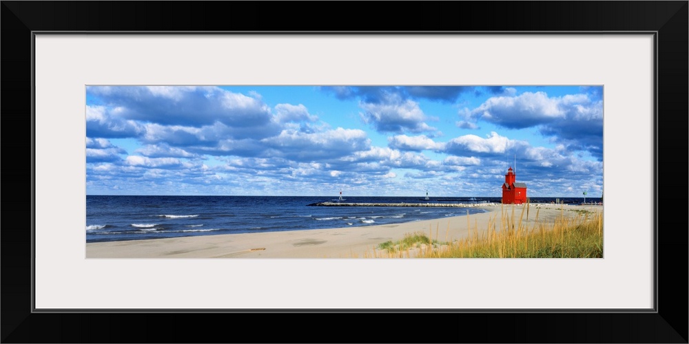 Panoramic photograph of a large lighthouse next to a dock on a sandy beach in Holland, Michigan during a sunny day.  The w...