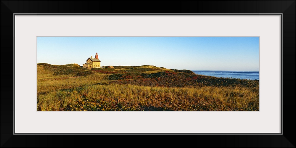 A large lighthouse is photographed in panoramic view surrounded by open grassy land.