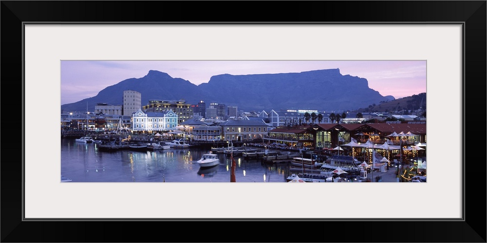 Panoramic photograph of busy boat dock lit up at dusk with skyline and mountains in the distance.