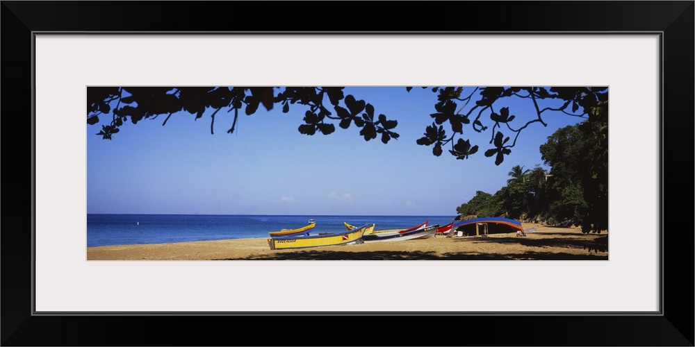 This is a panoramic photograph of boats on the sandy shore and framed with tropical foliage.