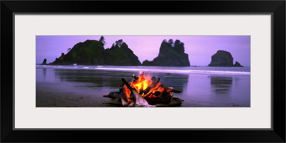 Panoramic photograph displays a small blaze as it sits contained on a sandy beach in the Northwest United States.  In the ...