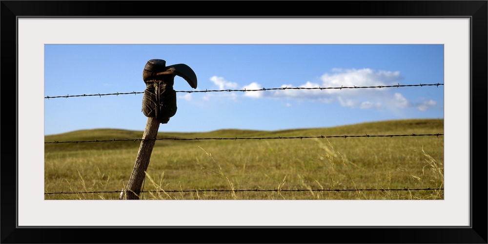 Panoramic photograph of cowboy boot hanging upside down on a cable fence with grass covered hills and a cloudy sky in the ...