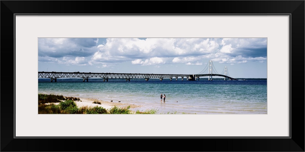 Panoramic picture of a massive bridge that stretches across a lake in Michigan. Some beach on the lake can be seen with tw...