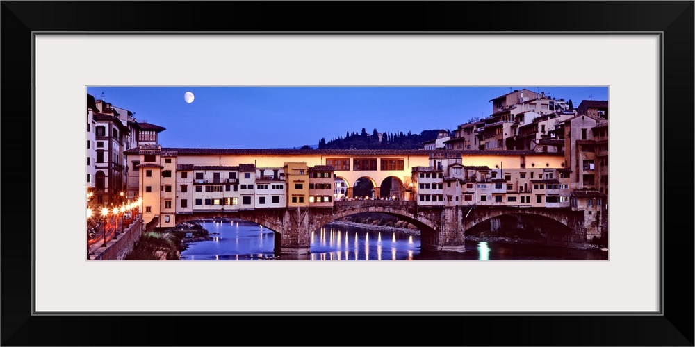 Panoramic photograph focuses on an overpass as it spans a wide river and the moon shines bright on this city at night.  Th...