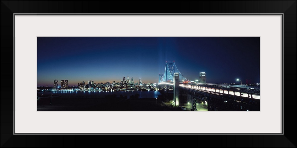 Late evening shot of a brightly lit Delaware Bridge crossing the Delaware River with the Philadelphia night skyline in the...