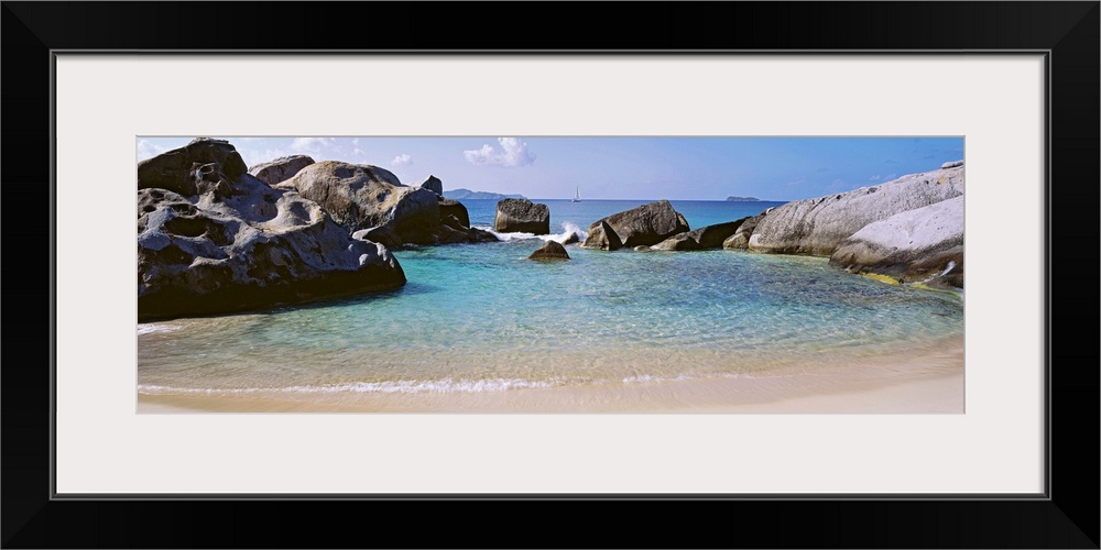 Panoramic photograph showcases an ocean traveling into a small cove surrounded by large formations of stones and slowly hi...