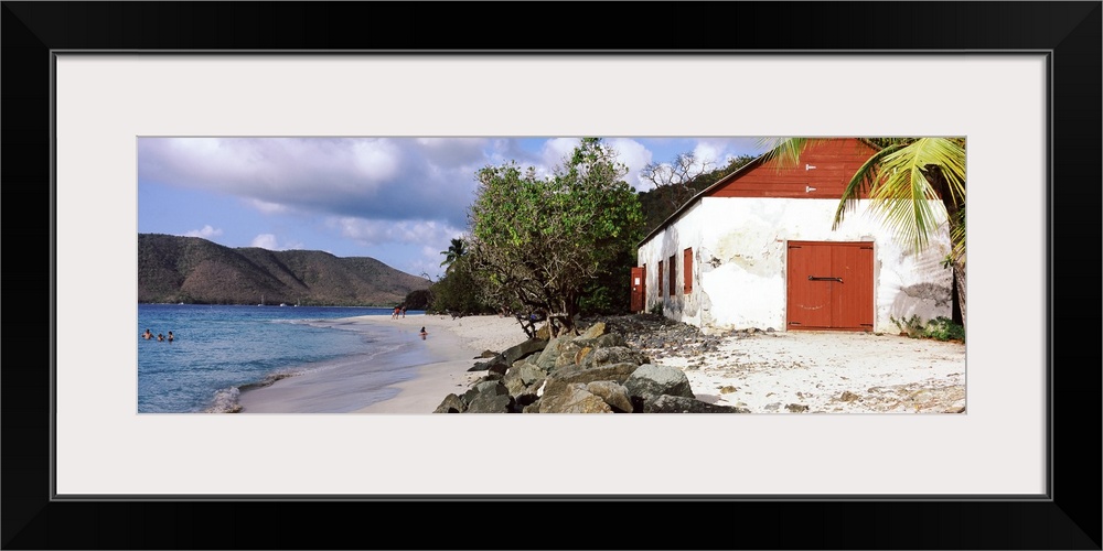 Wide angle photograph taken of a building sitting on a beach with rocks sitting just in front of it and the ocean with peo...