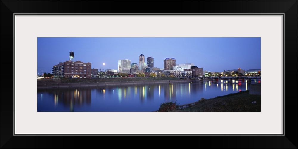 This panoramic photograph is taken of buildings lit up at night that sit on the water front in Des Moines and reflect in t...