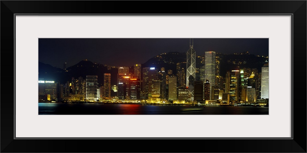 Panoramic photograph of the Hong Kong skyline, lit up at night, reflecting in the water, in China.