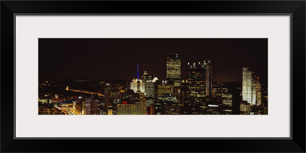 Horizontal, big, high angle photograph of the Pittsburgh skyline, with brightly lit buildings at night.