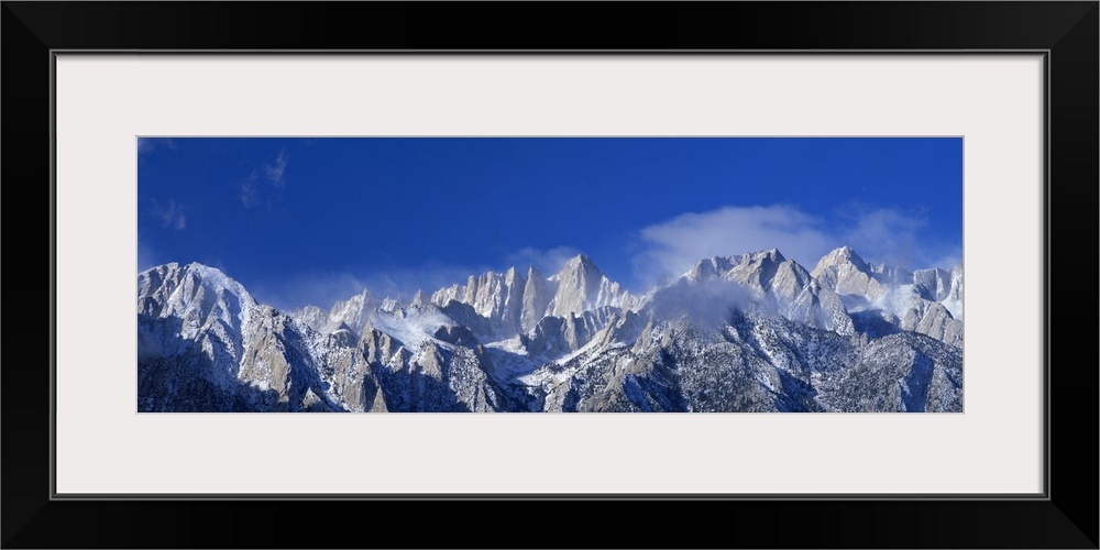 Panoramic photograph of snow covered Mount Whitney beneath a vibrant blue sky in California.