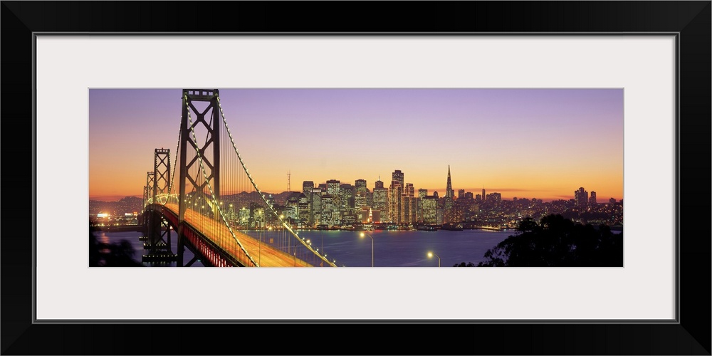 Twilight and the Golden Gate Bridge with the San Francisco Skyline with a purple and gold sky.