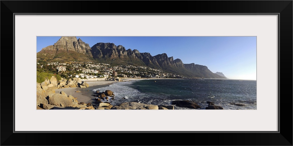 Panoramic photograph of shoreline with rocky cliffs and huge rock formations under a clear sky.