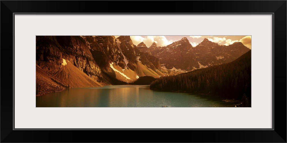 Panoramic photograph of waterfront surrounded by mountains under a cloudy sky.