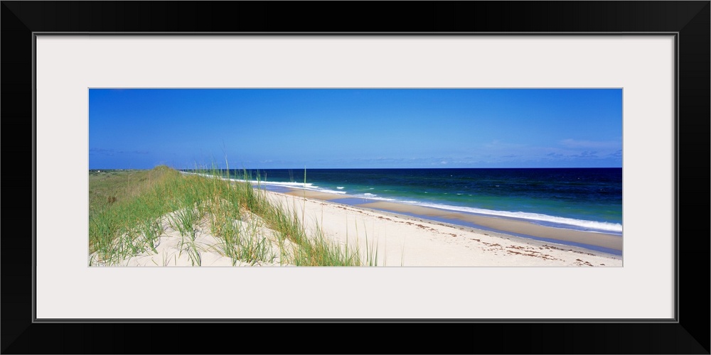 Panoramic photograph focuses on a long stretch of a sandy beach within North Carolina as the waves slowly come in and brea...