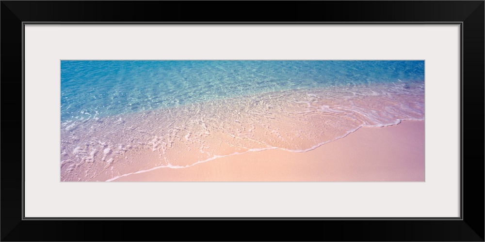 Panoramic photograph concentrates on a small section of clear ocean water as it gently washes onto a sandy shore.
