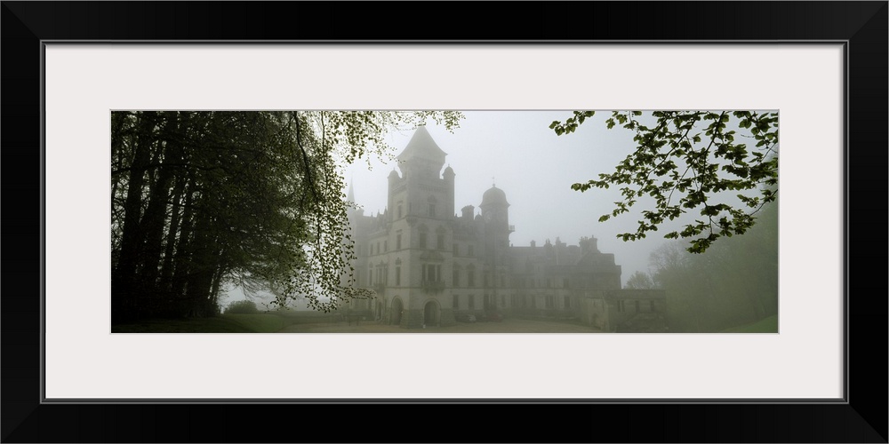 A large castle is faintly shown behind fog and surrounded by trees.