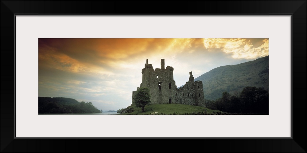 Panoramic photograph of stone palace on hillside at sunset.  There is water in the distance and the sky is cloudy.