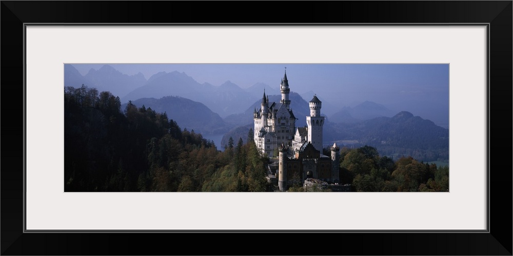 A grand historic castle sits perched at the top of a hill in Central Europe, amidst a forest of pine trees and tall mounta...