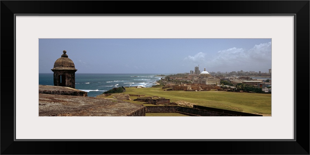 The coast of San Juan is photographed in panoramic view with the ocean to the left and the city on the right.