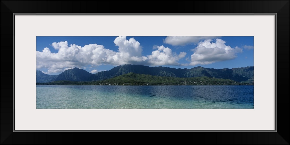 Panoramic photograph taken across the ocean looking at a Hawaiian island with immense clouds floating over.