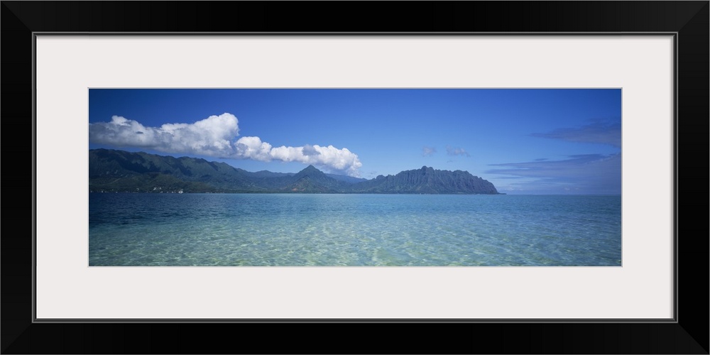 Panoramic view of the tropical ocean surface of the Pacific, with tall mountains and clouds on the horizon.