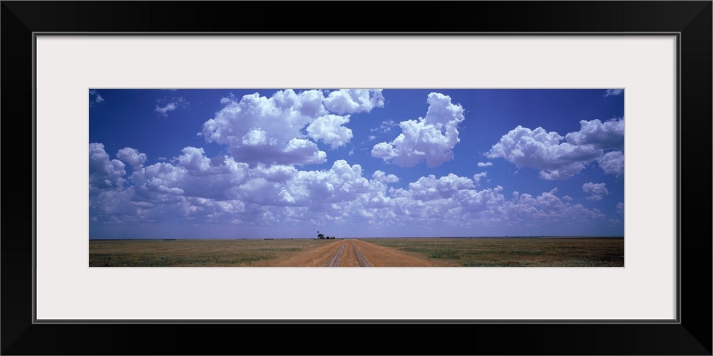 Panoramic photograph taken at the end of a dirt road with flat fields on both sides and large clouds hovering above.