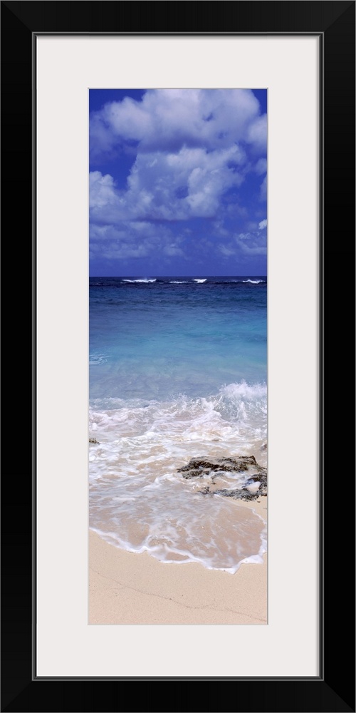 Vertical, large photograph of clear blue waters hitting the beach beneath a blue sky with billowing clouds in Island Harbo...