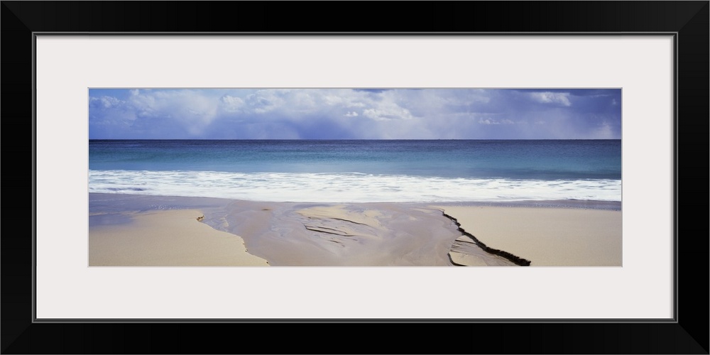 Wide angle shot from a deserted beach looking out onto the ocean under a cloudy sky.