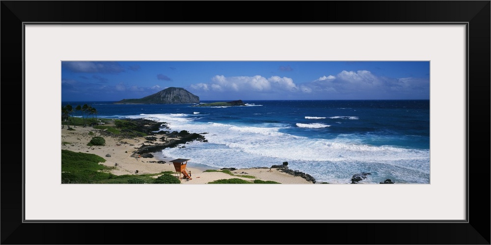 Waves crashing on the Makapuu Beach in Hawaii with an orange lifeguard tower look out over the water and palm trees blowin...