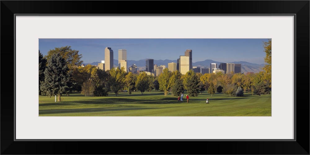 Big, panoramic photograph on the green of a golf course in Colorado, full of trees, the buildings of the Denver skyline in...