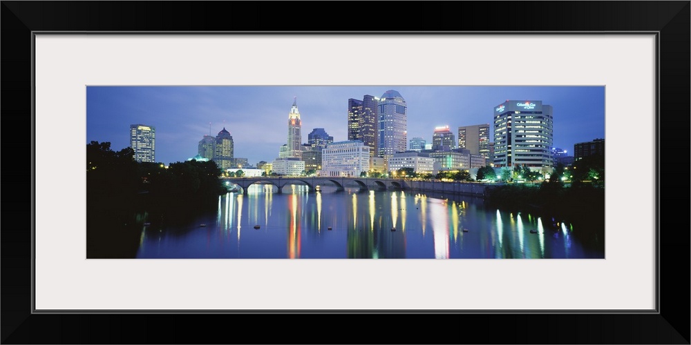 Giant, horizontal photograph of the Columbus skyline at night, reflecting in the waters of the Scioto River, past the Main...