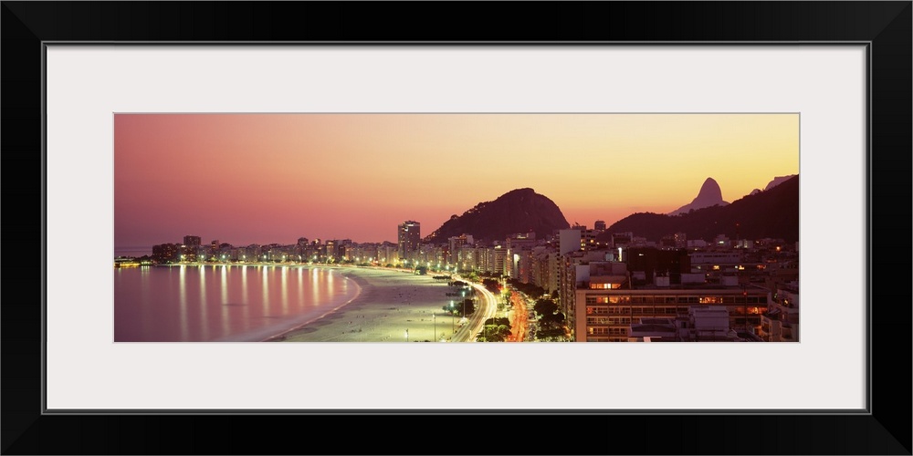 Giant landscape photograph of the curving shoreline of Copacabana Beach, lined with buildings that are lit at night, in Ri...