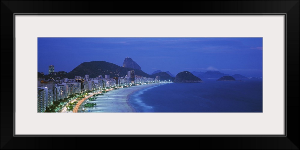 A large panoramic shot of the coast and skyline of Rio De Janeiro. Taken at dusk, the buildings and streets are lit up wit...