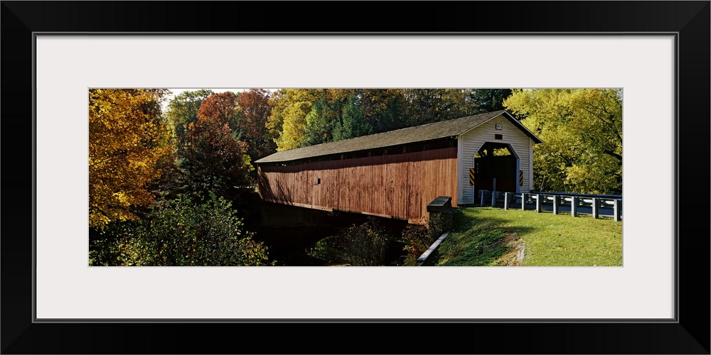 Panoramic photograph of the wooden McGees Mill covered bridge, surrounded by a forest of trees with fall foliage, in Clear...