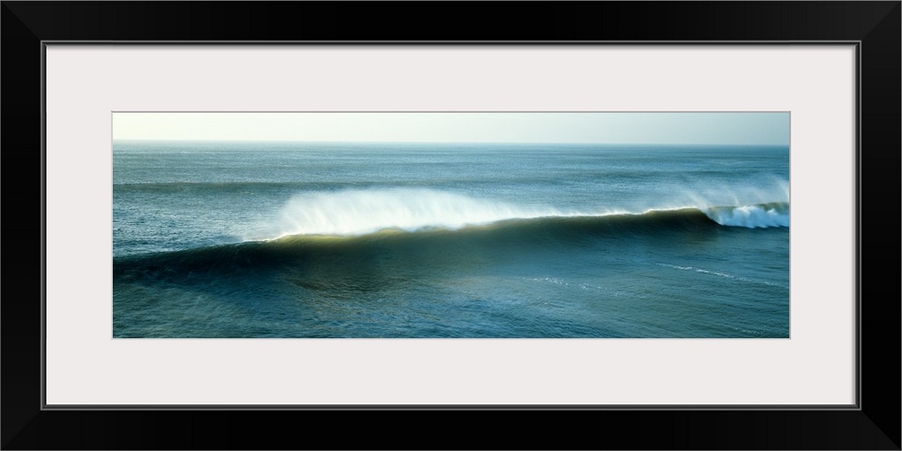 Wide angle view of an immense wave during sunrise that has begun to curl on the far right of the picture.